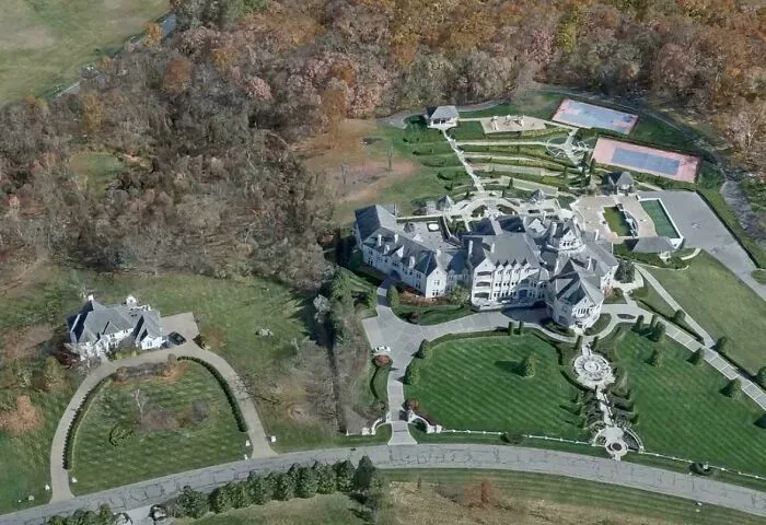 Aerial view of a large luxury estate with expansive lawns and recreational areas symbolizing consumerism excess.