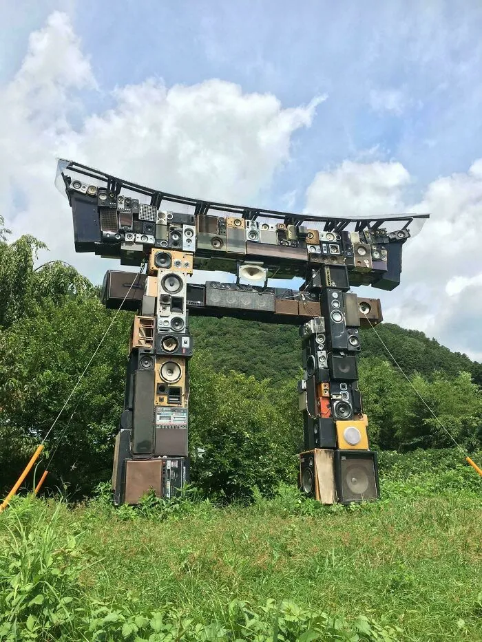 Torii gate constructed entirely from stacked speakers in an outdoor natural setting