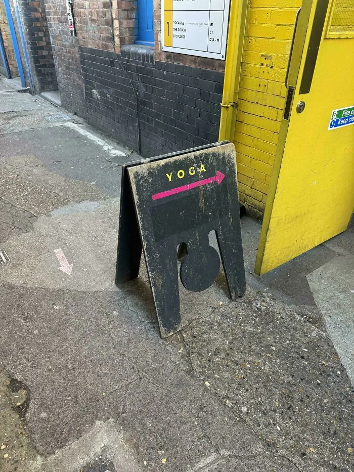 Worn sidewalk yoga sign with arrow pointing to entrance near yellow door