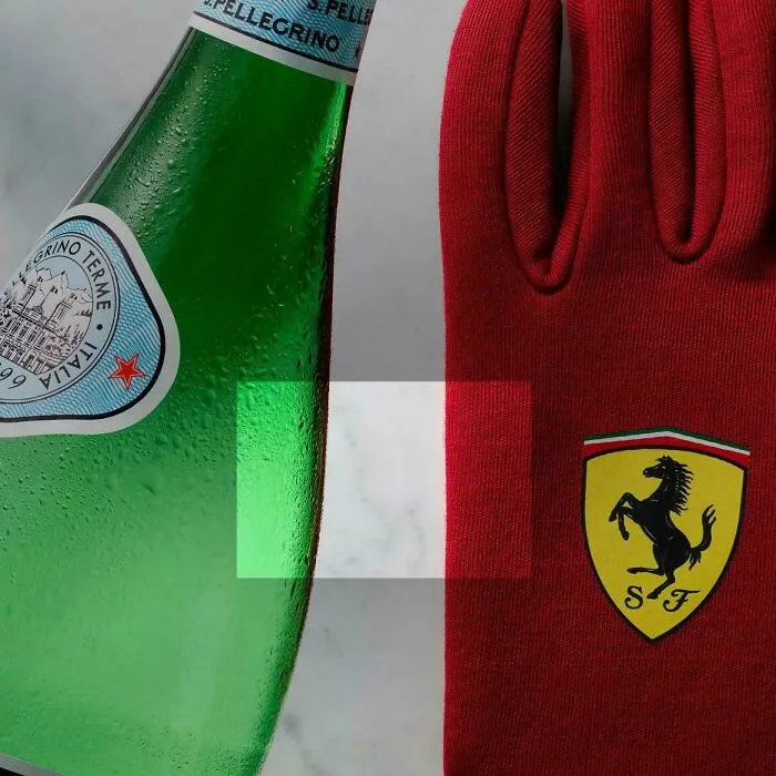 Close-up of red glove with Ferrari logo next to green glass bottle on marble surface