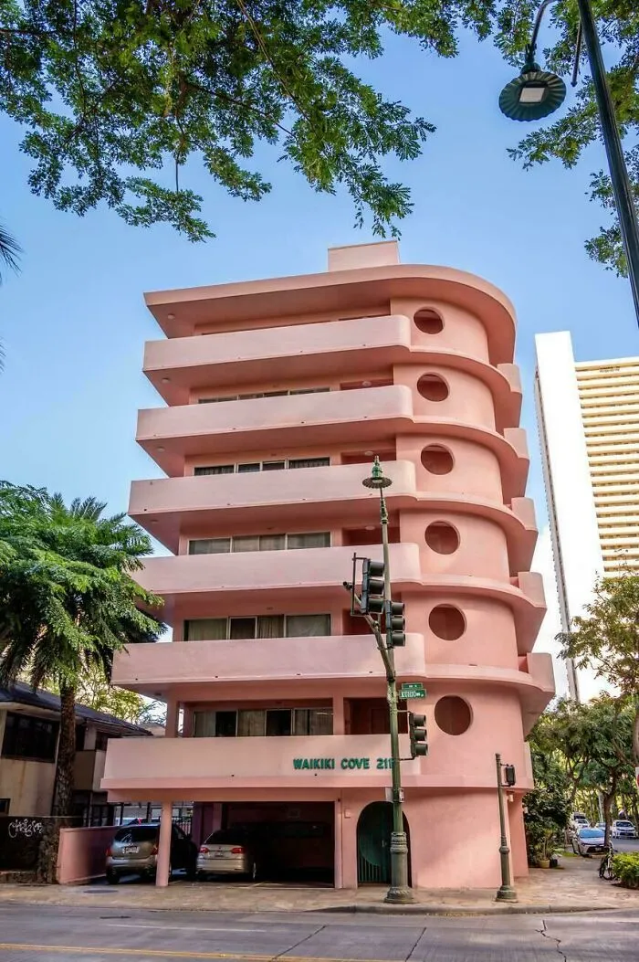 Pink modern curved building with circular windows and balconies under blue sky