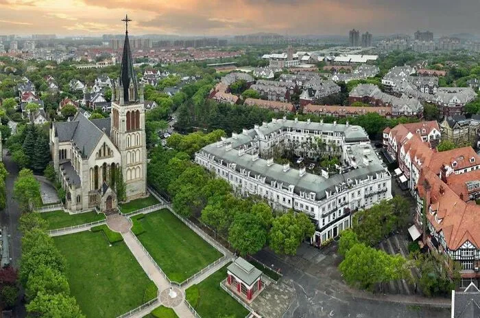 Aerial view of urban area with church and residential buildings surrounded by greenery in a modern cityscape.