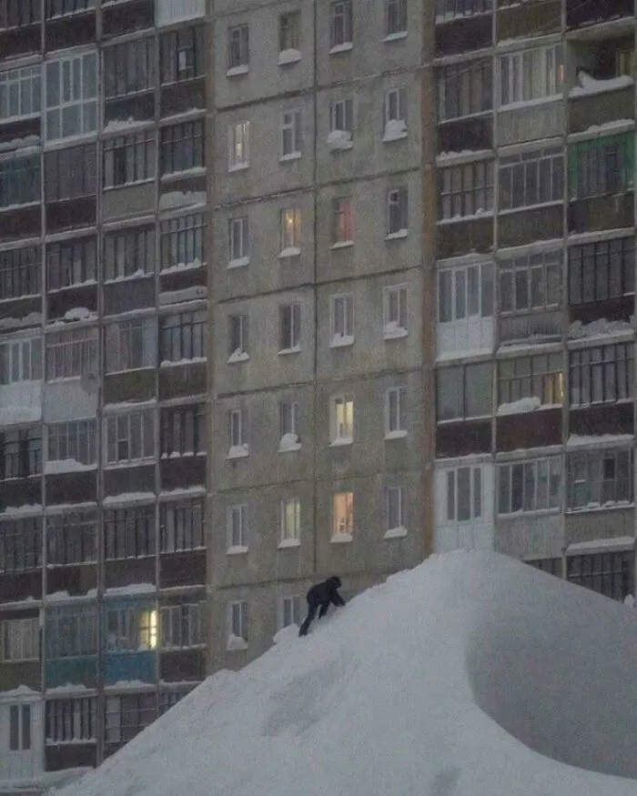 Person climbing large snow pile in front of gloomy urban apartment buildings showing dystopian urban hell.