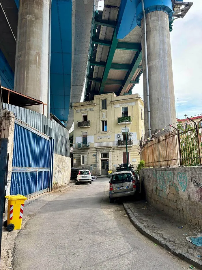 Dystopian urban hell scene with an old building under a massive highway overpass in a narrow city street.