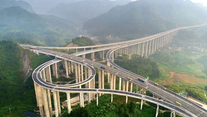 A complex urban highway interchange winding through green hills, illustrating dystopian urban infrastructure.