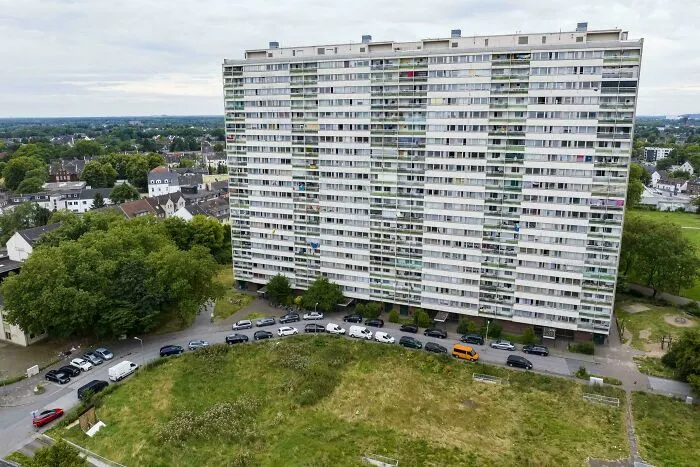 High-rise residential building in urban hell setting surrounded by greenery and parked cars showing modern life’s price.
