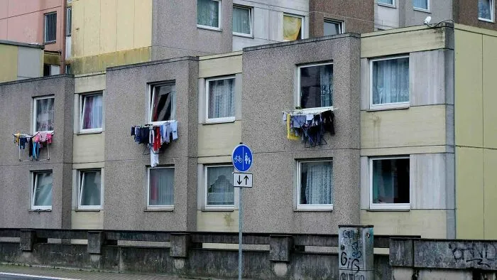 Dystopian urban hell with laundry hanging from windows on a grey concrete apartment building facade.