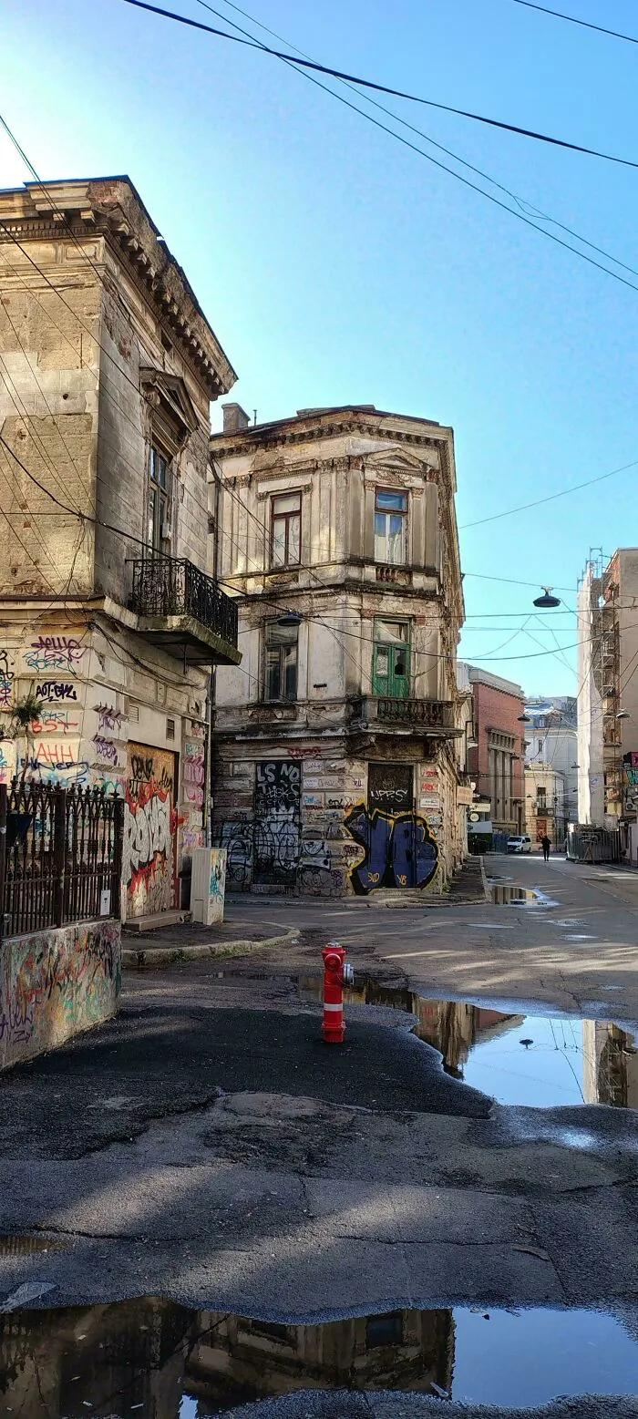 Dystopian urban hell scene with graffiti-covered old buildings, cracked pavement, and puddles reflecting a fire hydrant.