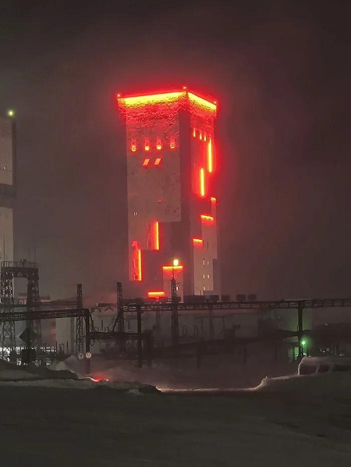Dystopian urban hell scene with glowing red lights on an industrial building under dark, foggy night conditions.