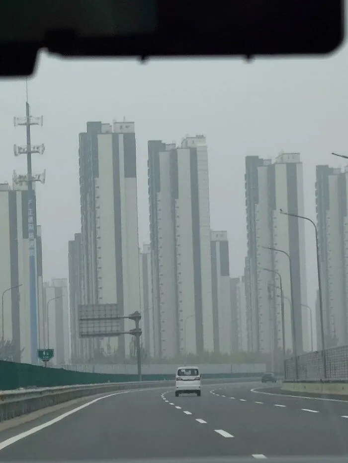 View of a dystopian urban hell with tall apartment buildings lining a foggy empty highway in modern city life.