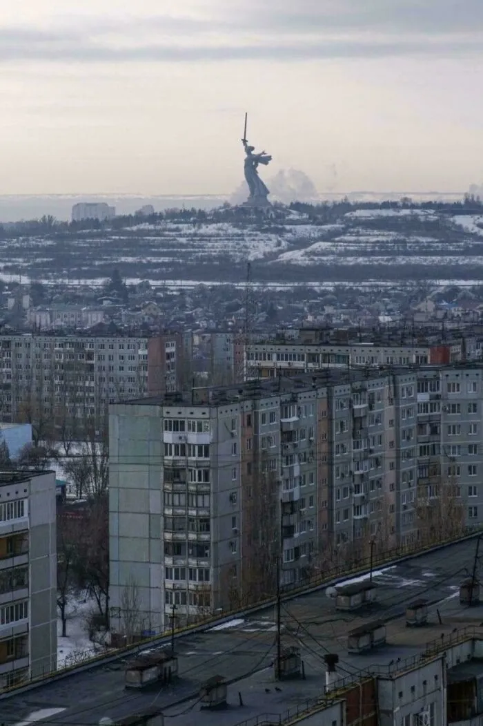 Urban hell scene with gray Soviet-era apartment blocks and a distant statue in a bleak, cold modern cityscape.