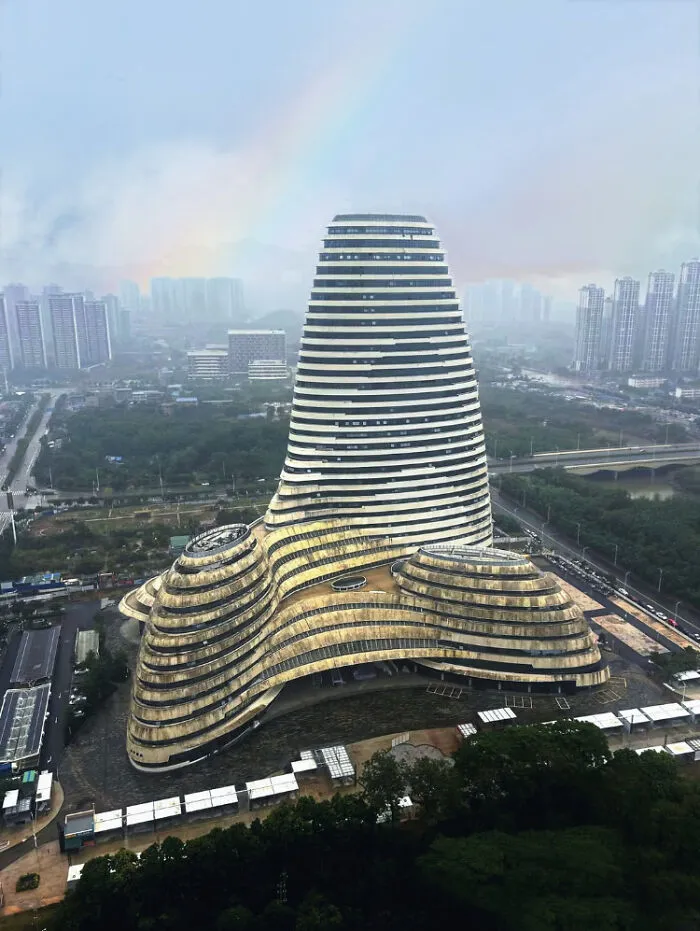 Futuristic urban hell building with layered architecture surrounded by cityscape under a gray, smoggy sky with a faint rainbow.