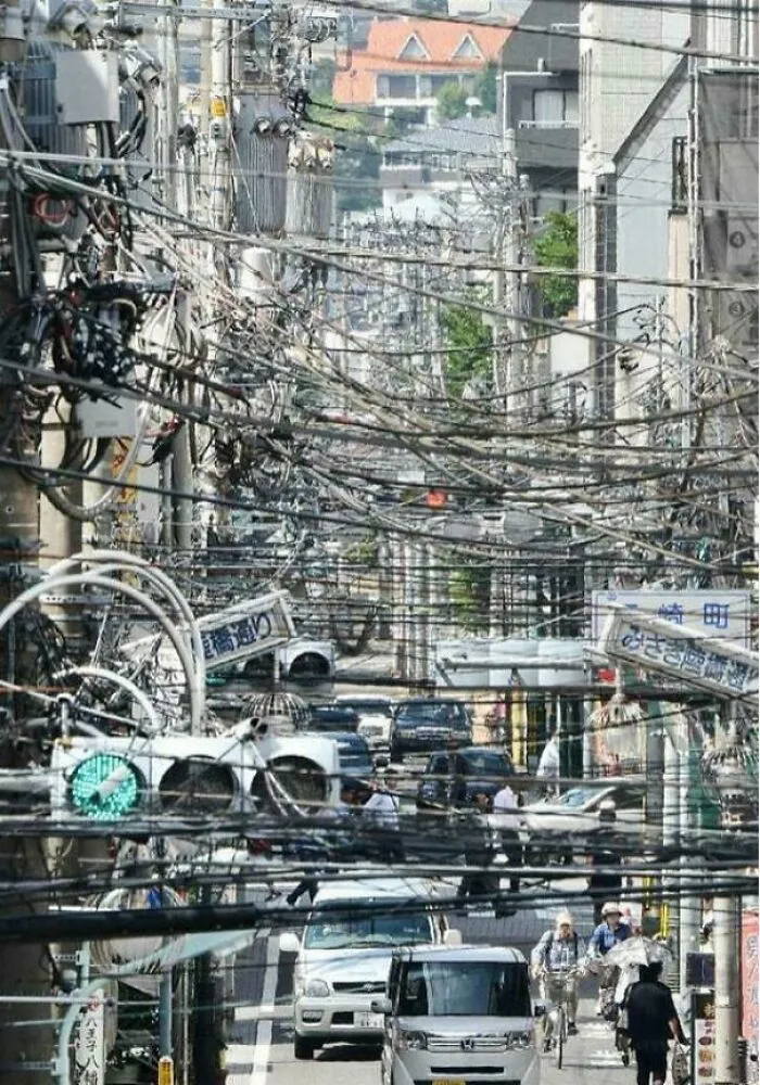 Busy urban street filled with tangled power lines, vehicles, and cyclists illustrating dystopian urban hell chaos.
