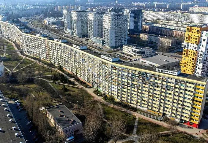 A dystopian urban hell scene showing large, repetitive apartment blocks and crowded cityscape illustrating the price of modern life.
