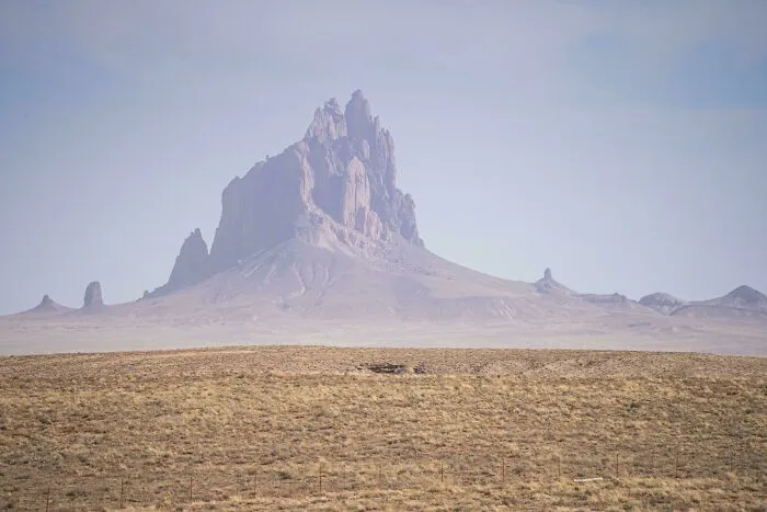An extremely large, jagged mountain peak rising from a vast, flat landscape, an eerie and scary natural formation.