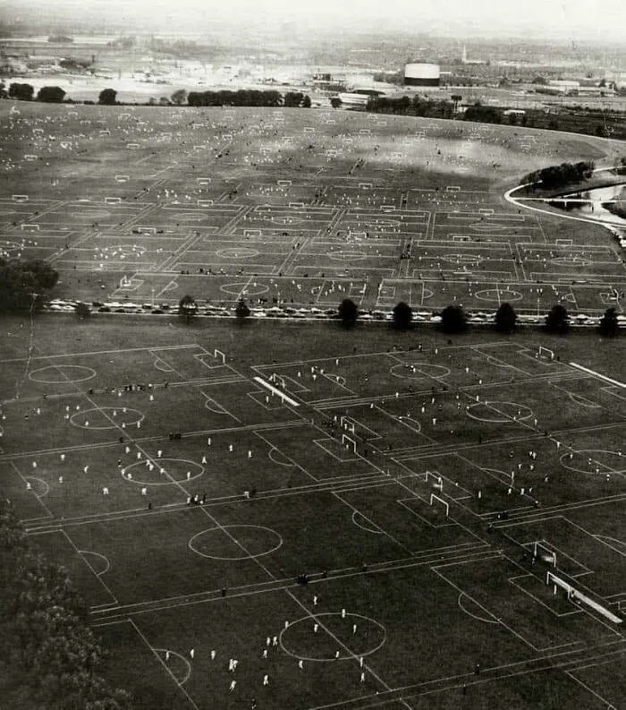 Aerial view of numerous soccer fields showing extremely large things and eerie scale with distant buildings.