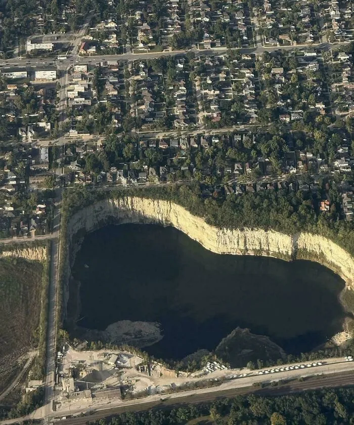 Extremely large things: An aerial view of a vast, scary, and eerie quarry or sinkhole beside a densely populated suburban area.