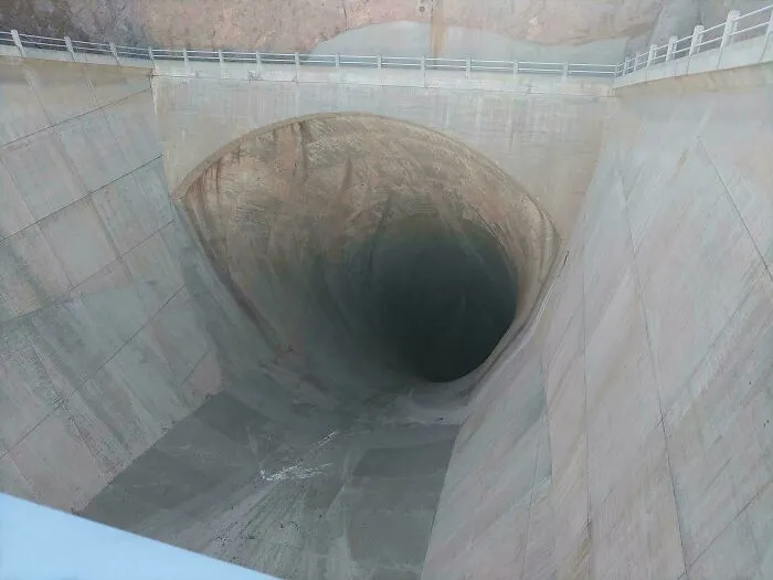 Extremely large things: A deep, eerie, and scary concrete spillway, appearing as a massive void in a dam structure.