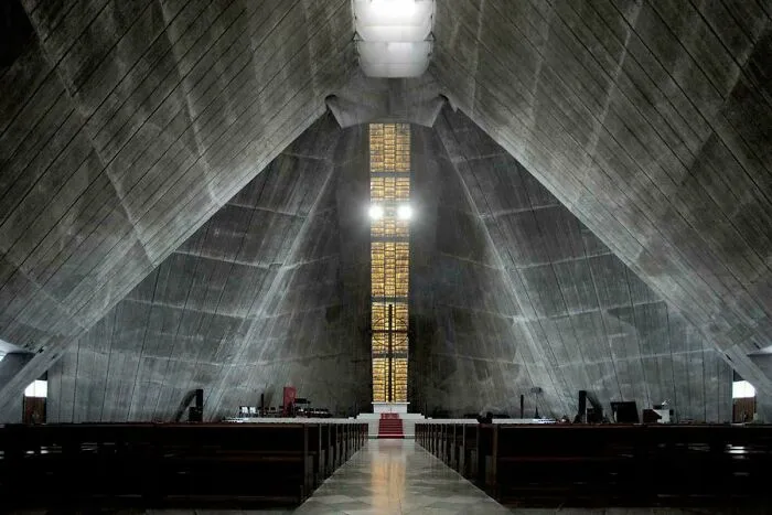 Extremely large and eerie concrete church interior with a cross-shaped stained-glass window, creating a scary sense of vastness.
