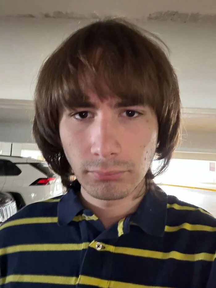 A young man with an unfortunate shaggy brown haircut and bangs, wearing a striped polo shirt.