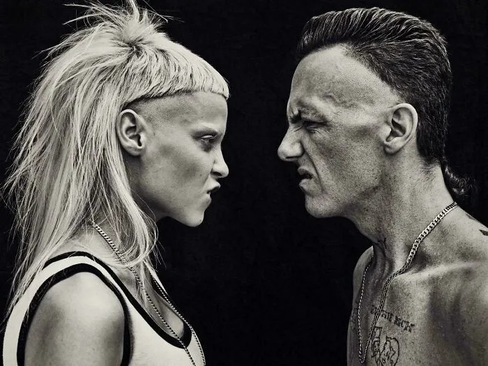 A man and a woman face each other, both with severe and unfortunate haircuts.