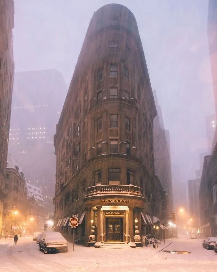 A beautiful, snow-covered triangular architecture of a building, Delmonico's, lit up at night, creating an unreal scene.