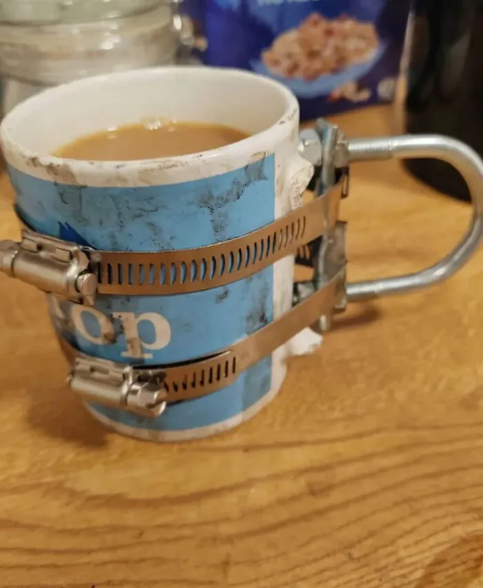 Coffee mug repaired with metal clamps and a pipe handle showcasing redneck engineering creativity and resourcefulness.