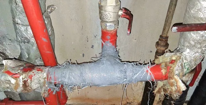 Rusty and patched red pipes held together with tape and wires, an example of redneck engineering plumbing fix.