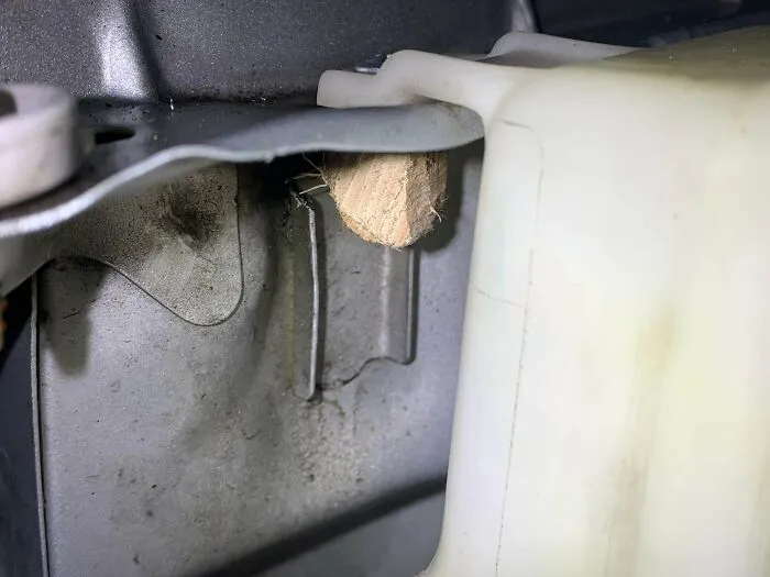 Close-up of redneck engineering using a wood wedge to secure a metal car part inside the engine compartment.