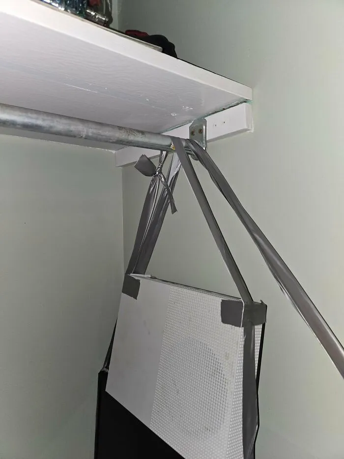 Improvised redneck engineering solution using duct tape to hang a gaming console on a closet rod, risking damage.