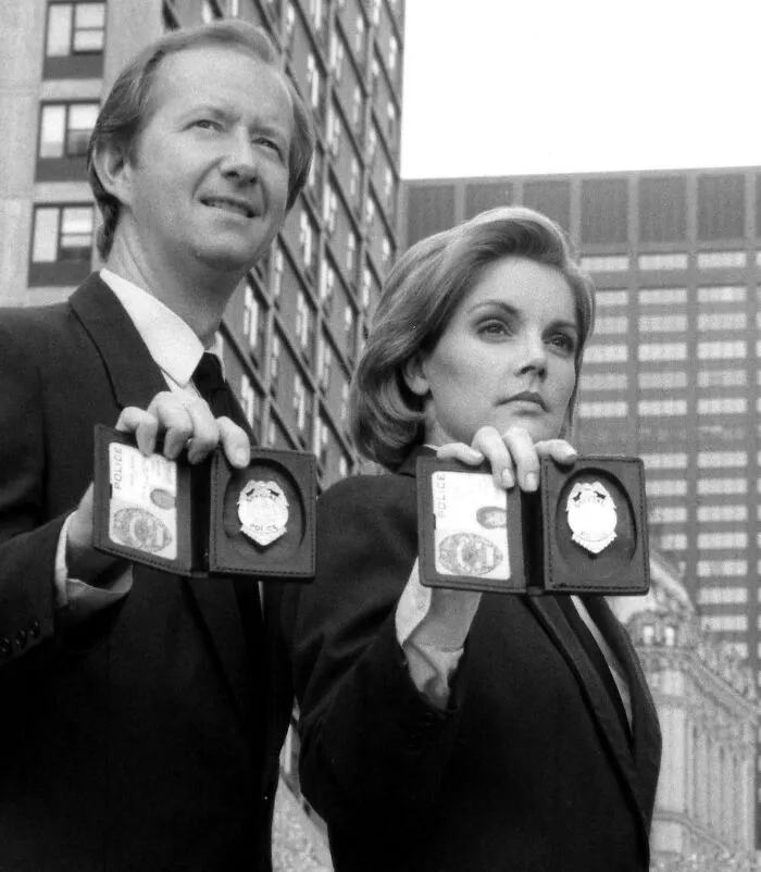 Two detectives holding up police badges in a black and white ’90s scene, evoking childhood memories and nostalgia.