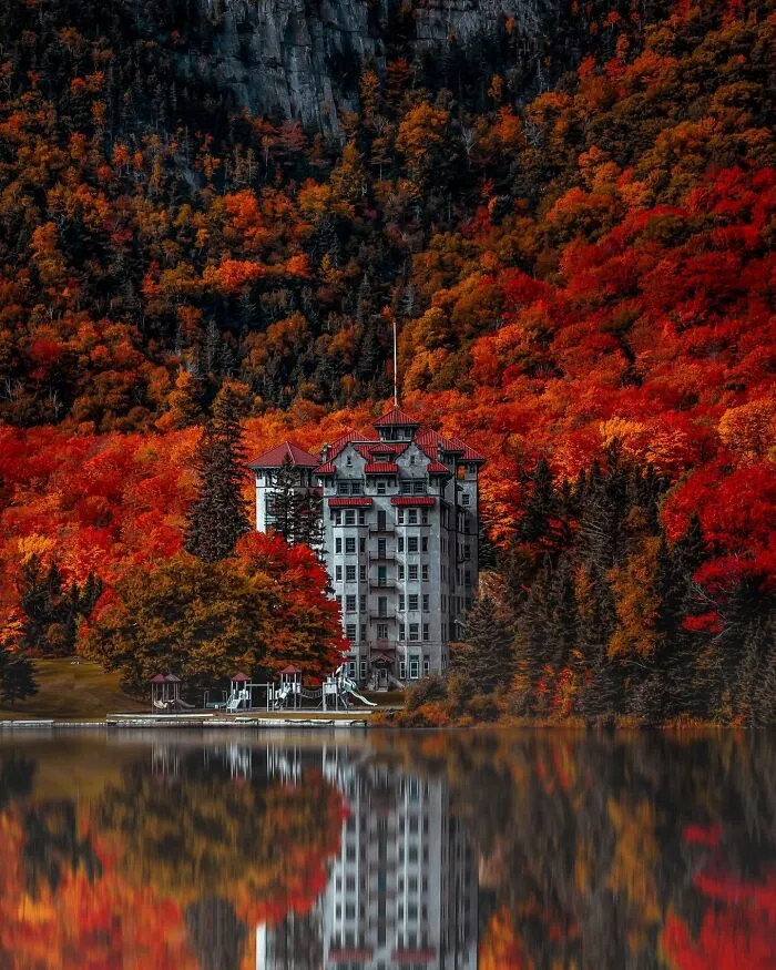 Stunning architecture of a grand building surrounded by vibrant autumn foliage, reflected in a still lake.