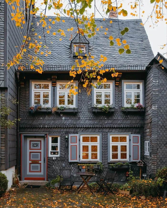Quaint German architecture with dark shingle siding, white windows, and yellow autumn leaves.
