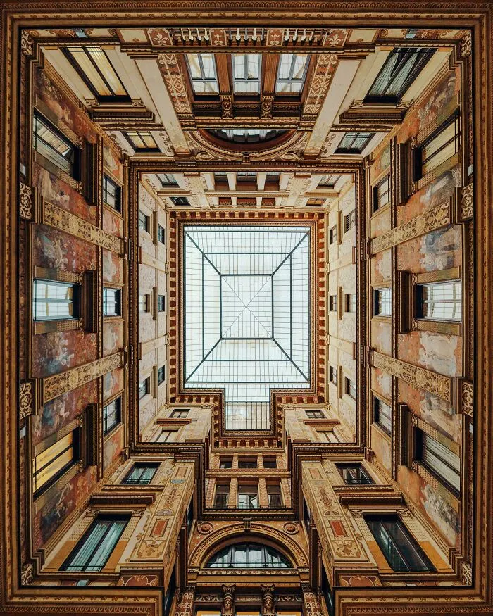 Looking up at symmetrical architecture of a building's inner courtyard with a large glass ceiling.