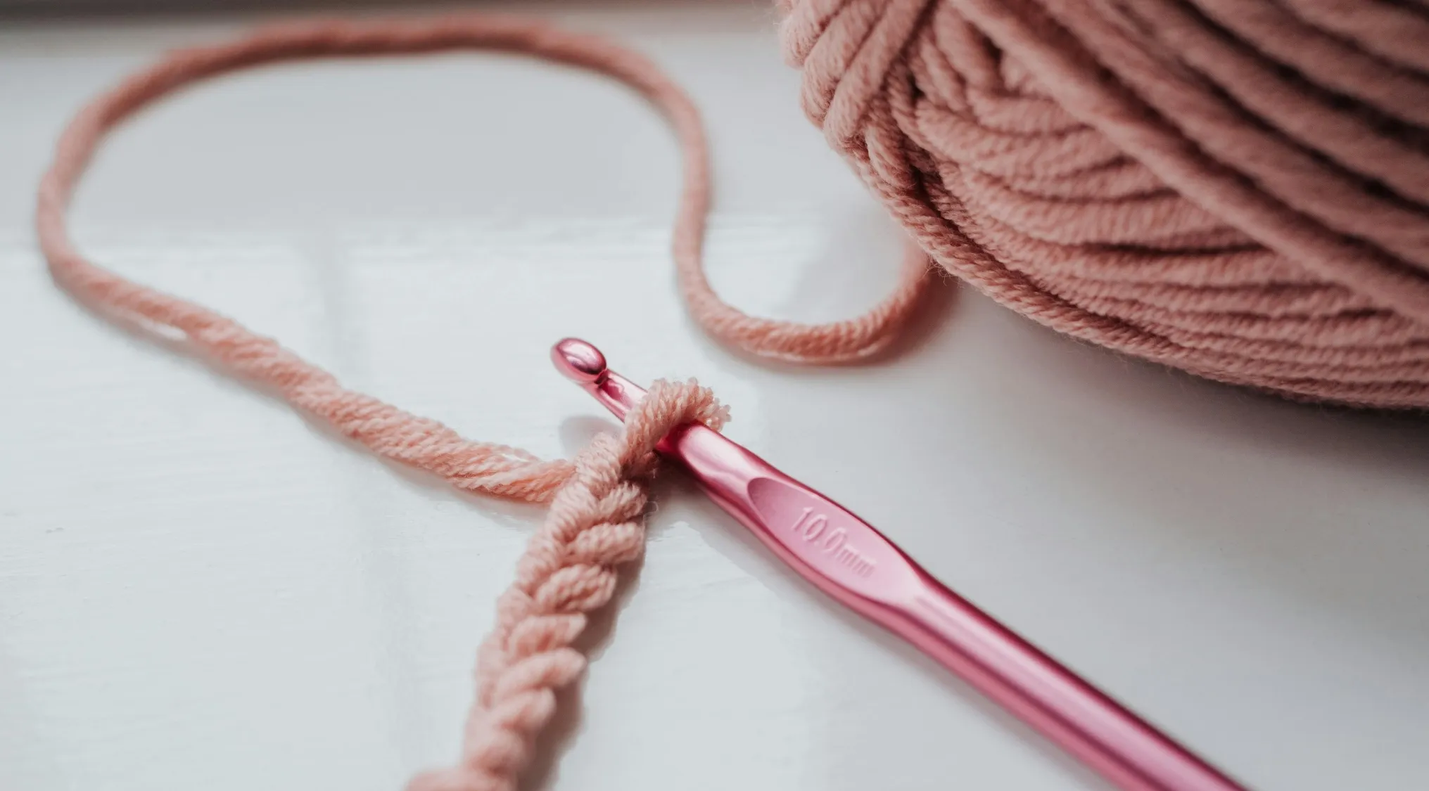 Pink crochet hook with yarn and partially crocheted wool, illustrating wool length measurement for UK 11+ school test.