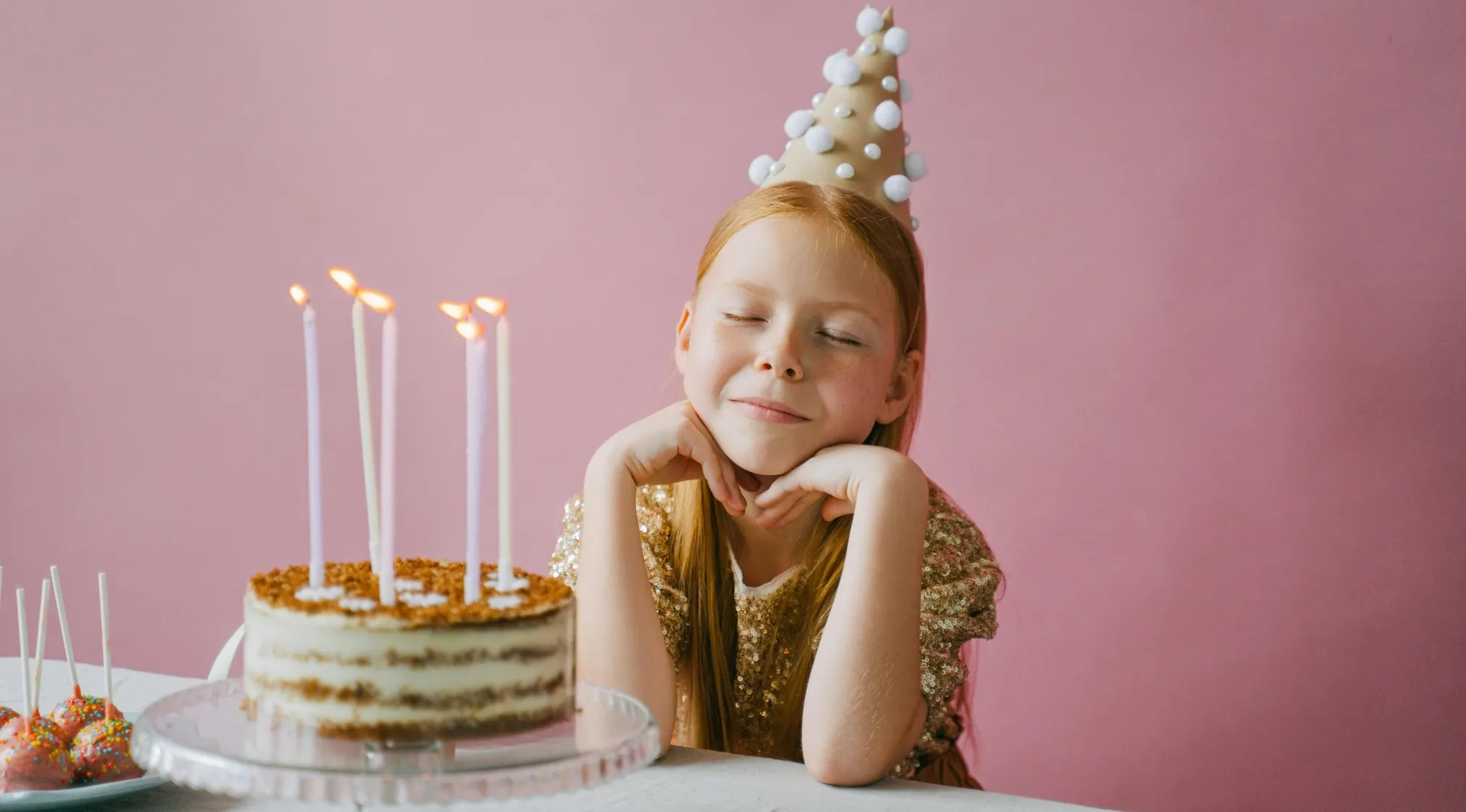 Young girl wearing a party hat sitting by a birthday cake cut into eight equal pieces for UK 11+ school test fraction question.