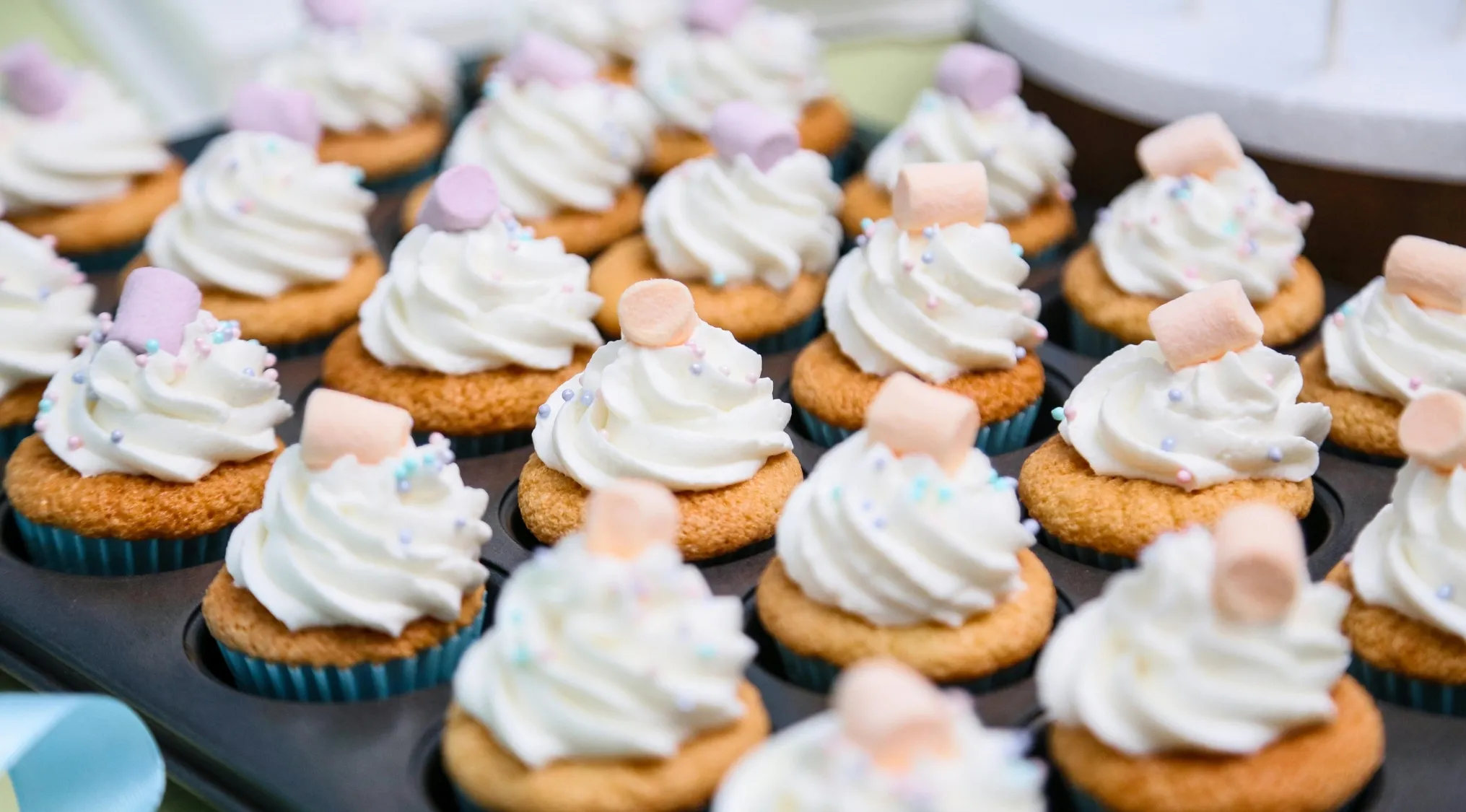 22 cupcakes with white frosting and colorful marshmallows in a tray, related to UK 11+ school test math question.