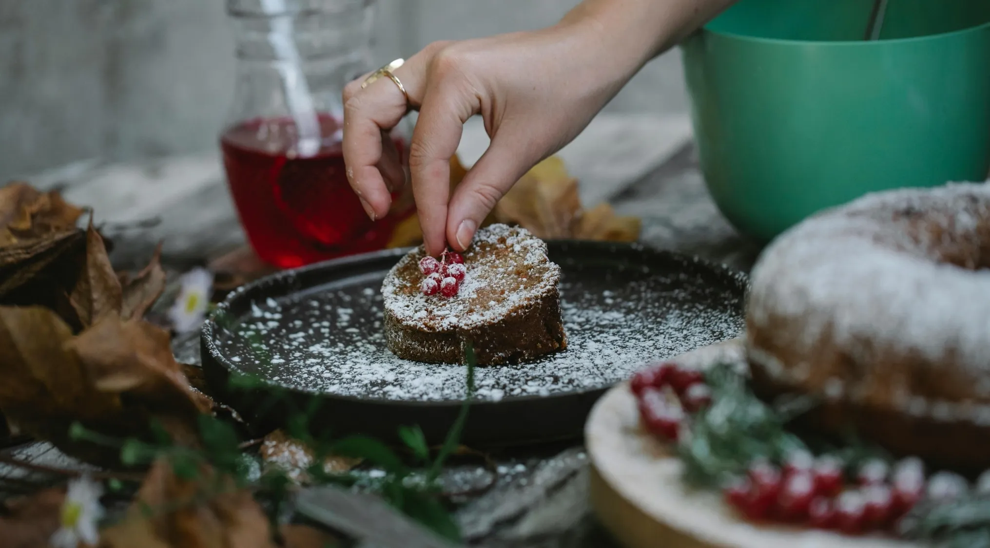 Hand decorating a cake with berries and powdered sugar during a charity bake sale for UK 11+ school test.