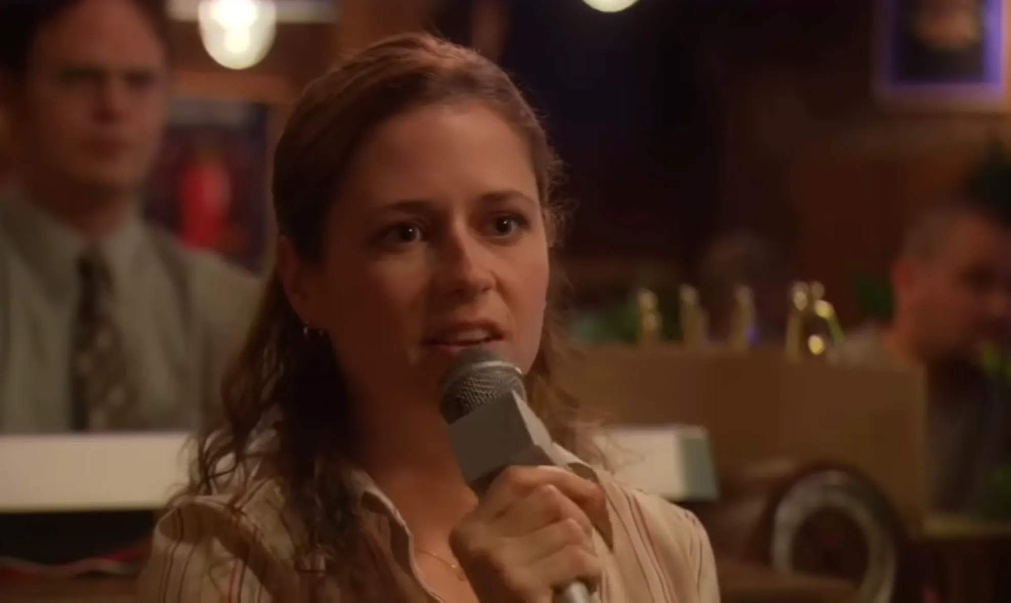 Pam Beesly speaking into a microphone in a casual setting, known as receptionist and office administrator in The Office.