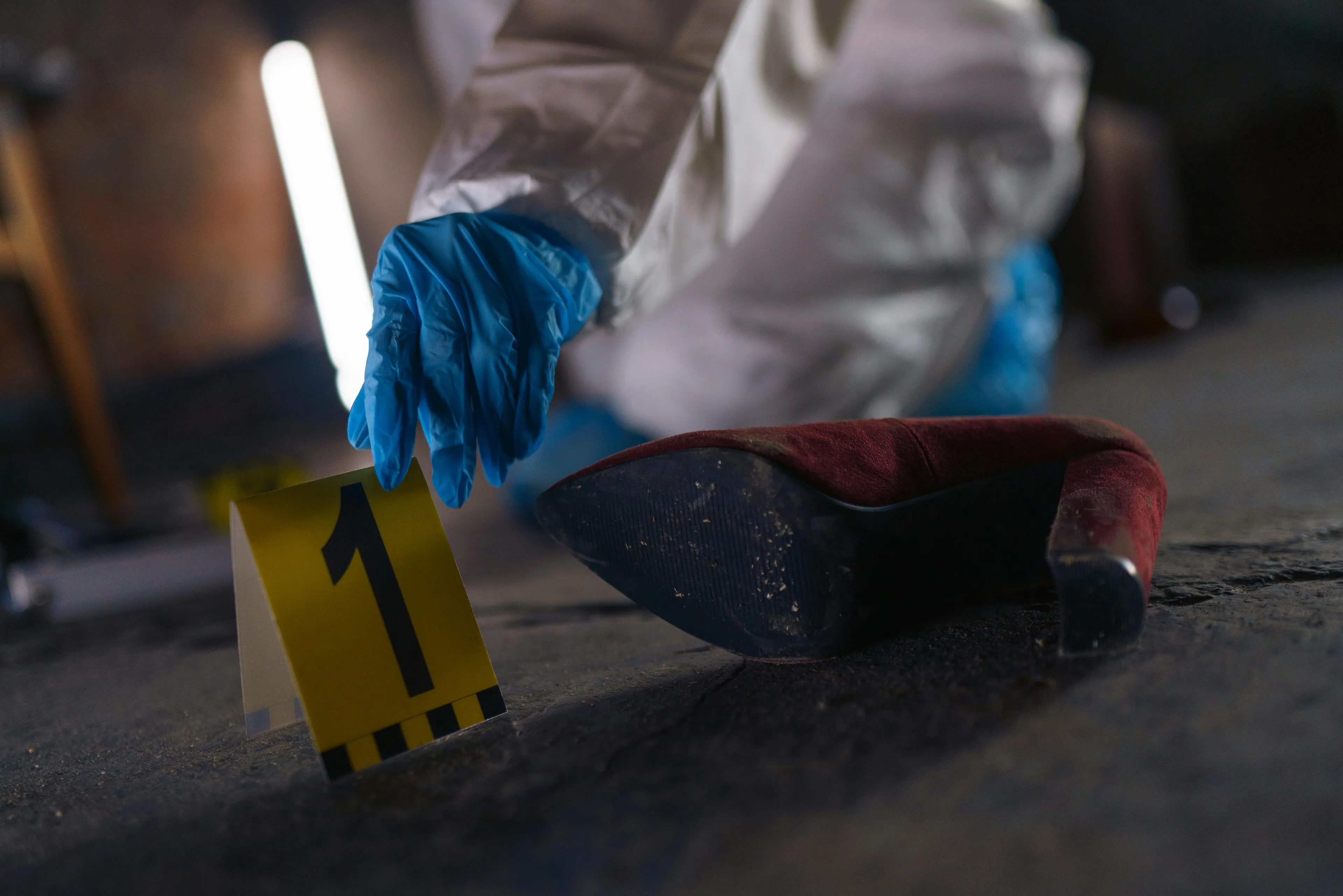 Forensic science crime scene investigation with medical examiner placing evidence marker near red high heel shoe.