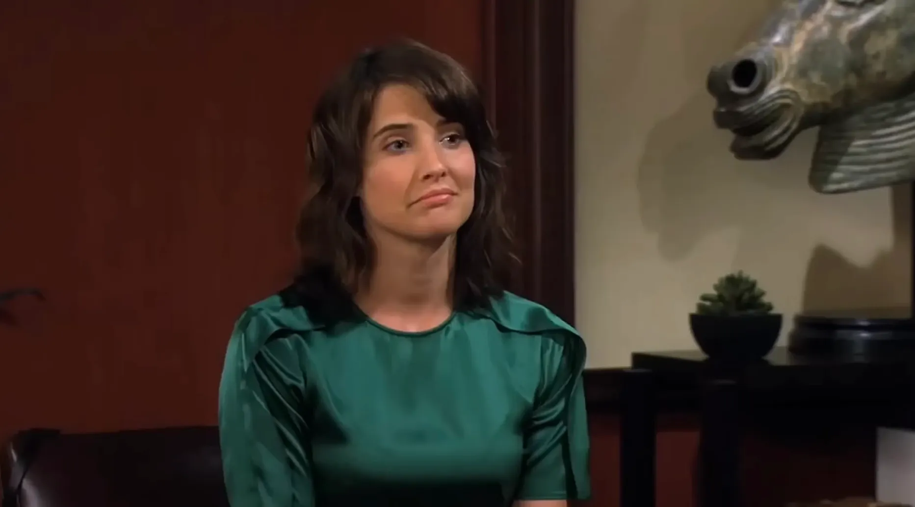 Young woman in green blouse sitting indoors beside a horse head sculpture, representing teen daughter character Lorelai.