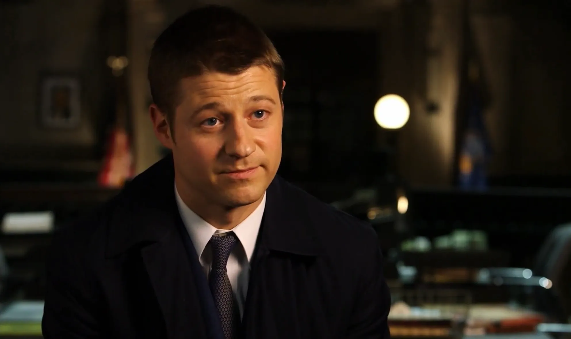 Ben McKenzie in a dark suit and tie, seated indoors, portraying a morally conflicted character in Breaking Bad.