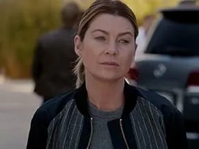 Woman portraying Meredith Grey in Grey's Anatomy standing outdoors near a car, wearing a casual jacket and serious expression.