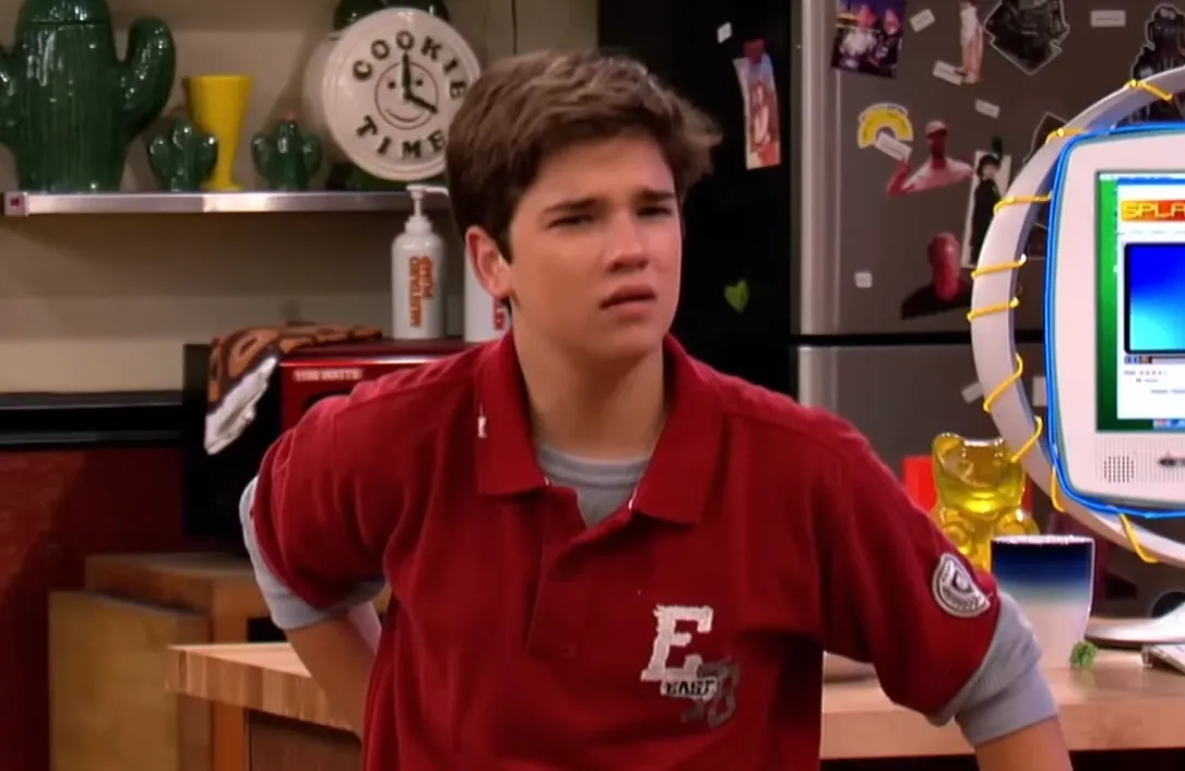 Teen boy in a red shirt looking confused in a kitchen setting, representing Phoebe's long-lost half-brother Freddie Benson.
