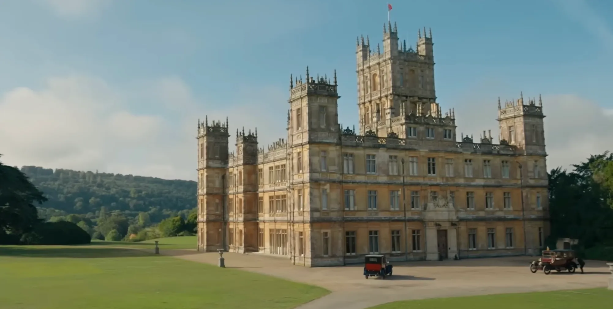Historic British period drama mansion surrounded by greenery with vintage cars representing TV shows Downton Abbey.