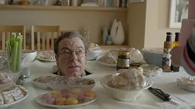 A man’s head appears on a dining table surrounded by covered dishes in a scene from the drama series about social media con artist Delvey.