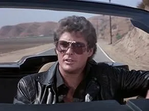Man wearing sunglasses and a leather jacket driving a car in a spy thriller cat-and-mouse chase scene.