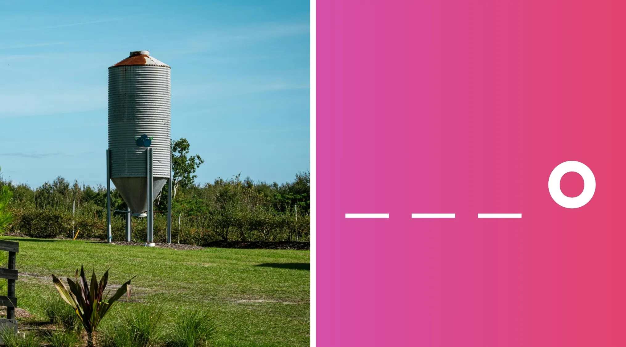 Metal grain silo standing outdoors on a farm with green grass and a clear blue sky background.