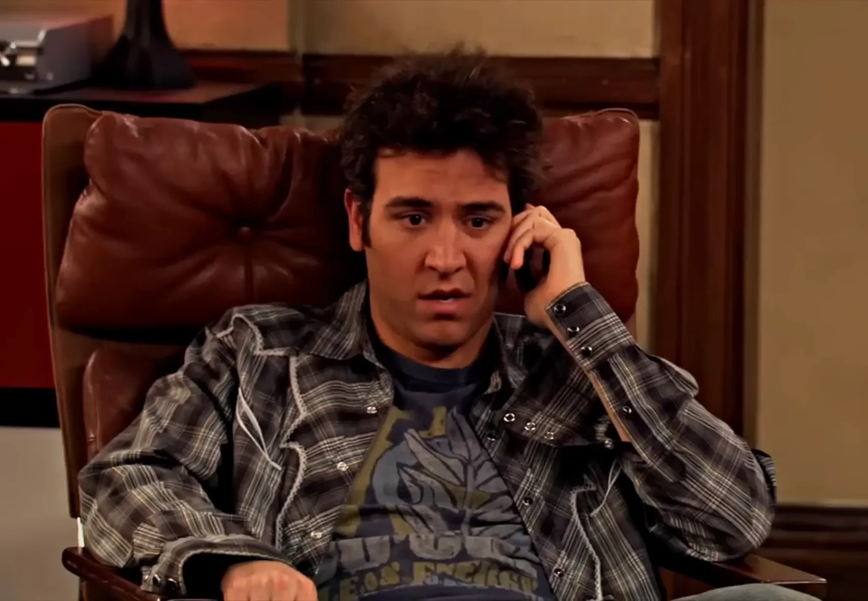 Ted Mosby from How I Met Your Mother sitting on a chair, talking on the phone during a casual moment indoors.