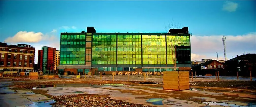 Modern green glass building with empty lot in foreground, representing sci-fi thriller TV shows about virus conspiracies.